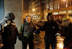 Andrew Costello, second from left, leads a prayer on the night of Feb. 21 as members of Operation Leftover take to the streets of downtown Indianapolis to provide food, clothing and conversation with people who are homeless. The group of young adult Catholics dedicated to helping the homeless is based at St. John the Evangelist Parish in Indianapolis. Costello prays with a man who is homeless, left, and two other members of the group, Michael Gramke, second from right, and Kellye Cramsey. (Photo by John Shaughnessy)