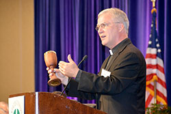 Holy Cross Father Daniel Groody stands before the U.S. bishops on June 14 and holds up a chalice handcrafted primarily with wood from a refugee boat that landed upon the beaches of Lampedusa. (Photo by Natalie Hoefer)