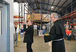 Archbishop Charles C. Thompson blesses the new Catholic Charities Terre Haute Foodbank building with holy water during a ceremony marking the opening of the facility on April 29. Assisting him is Conventual Franciscan Father Martin Day, pastor of St. Benedict Parish in Terre Haute. (Photo by Natalie Hoefer)