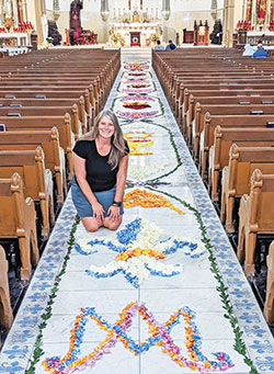 Caris Roller kneels on June 19 in the center aisle of St. John the Evangelist Church in Indianapolis surrounded by flower petals she placed there to make a variety of eucharistic and other faith-filled images, following a centuries-old Corpus Christi custom found in many European countries. The images were made at St. John for a holy hour that concluded the start of the National Eucharistic Revival in the archdiocese. (Submitted photo)