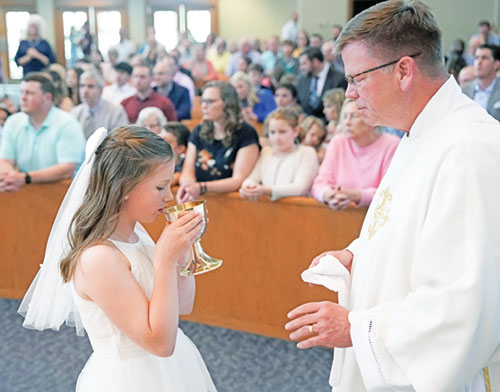 Elle Dalesandro of St. Simon the Apostle Parish in Indianapolis receives the Eucharist from Deacon James Wood as part of her first Communion at the parish church this spring. (Photos courtesy of Jennifer Driscoll Photography)